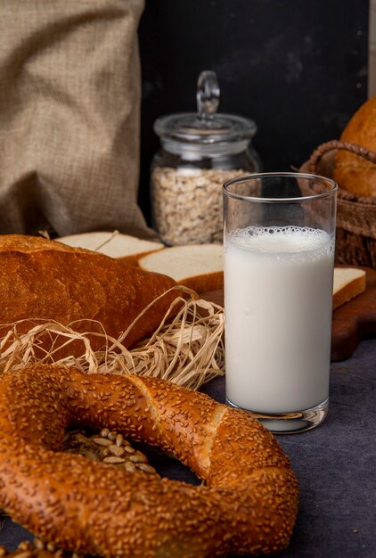 Side view of glass with milk and bagel on maroon surface and black background