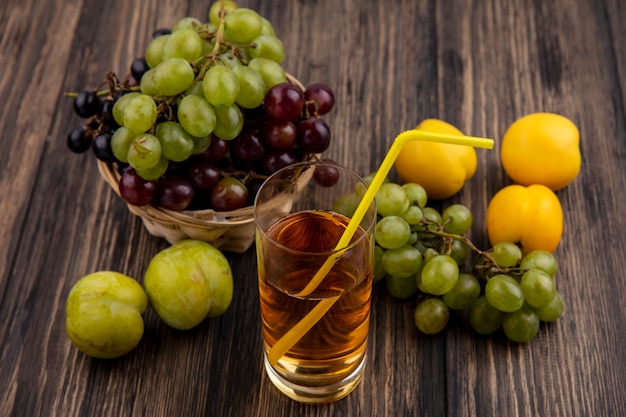 Side view of grape juice in glass and grapes in basket with pluots and nectacots on wooden background