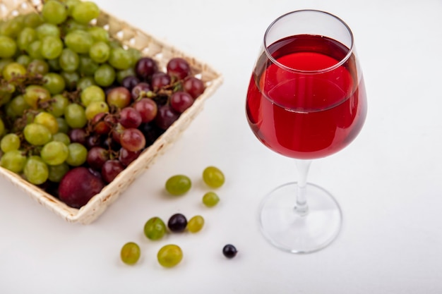 Foto gratuita vista laterale del succo d'uva nel bicchiere da vino e cesto di pluot e uva con acini d'uva su sfondo bianco