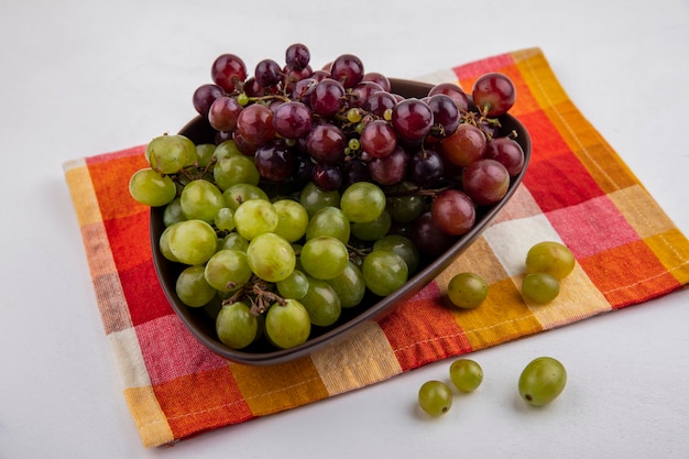 Side view of grapes in bowl on plaid cloth and on white background