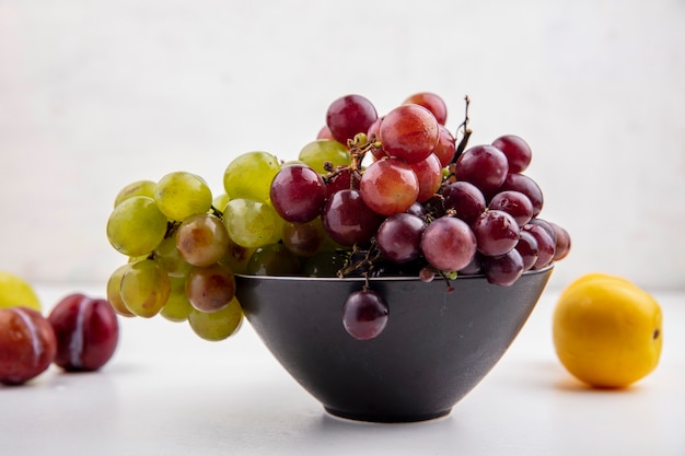 Side view of grapes in bowl with pluots and nectacot on white background