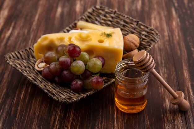 Вид сбоку виноград с сортами сыров и орехов на подставке с медом в банке на деревянном фоне