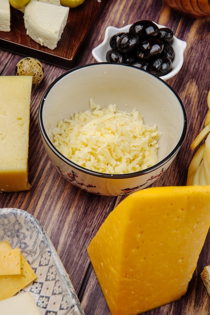 Vista laterale di formaggio olandese grattugiato in una ciotola e olive marinate nere su legno rustico