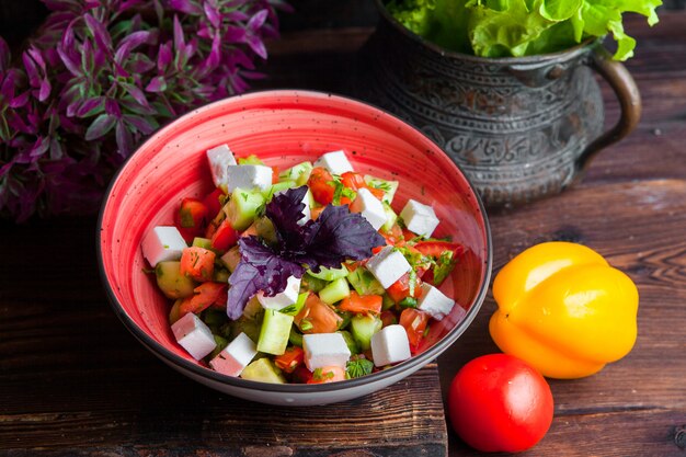 Вид сбоку греческий салат, помидоры, сыр фета, огурцы, маслины, фиолетовый лук на темном деревянном столе