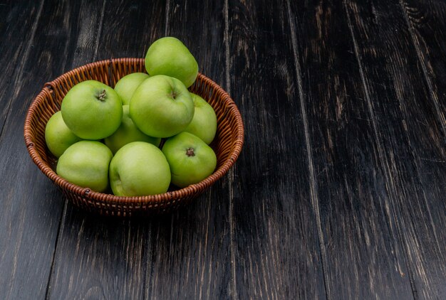 side view of green apples in basket on wooden background with copy space