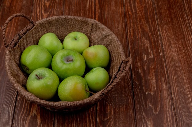 Side view of green apples in basket on wooden surface with copy space