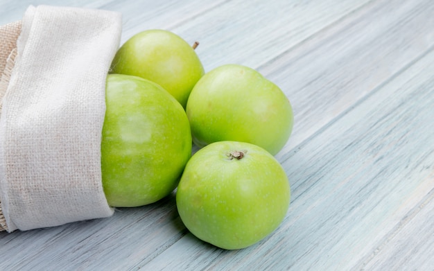 Side view of green apples spilling out of sack on wooden surface with copy space