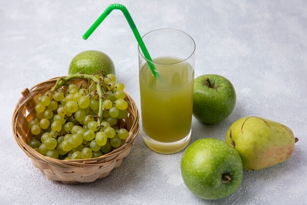 梨青リンゴと白い背景の上のガラスの緑のわらとリンゴジュースとバスケットの緑のブドウの側面図