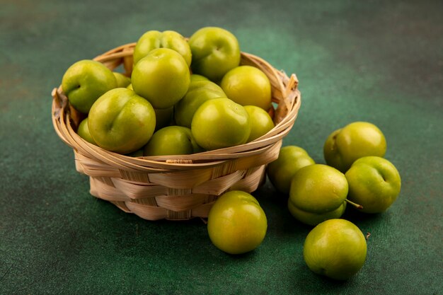 Side view of green plums in basket and on green background