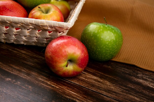 Side view green and red apples in a basket on a brown towel on a wooden background