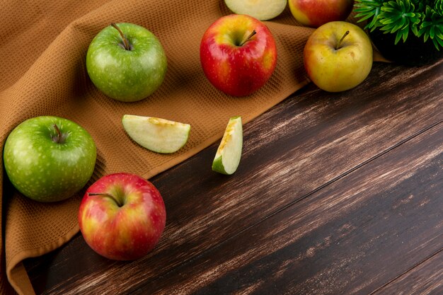 Вид сбоку зеленые и красные яблоки на коричневом полотенце на деревянном фоне