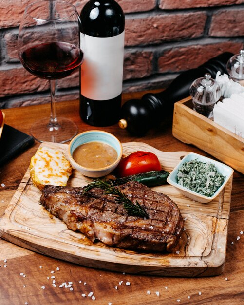 Side view of griled beef steak served with vegetables and sauce on wooden board