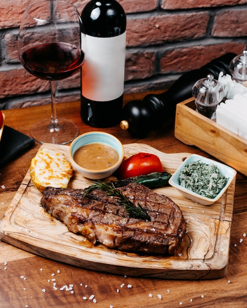 Side view of griled beef steak served with vegetables and sauce on wooden board