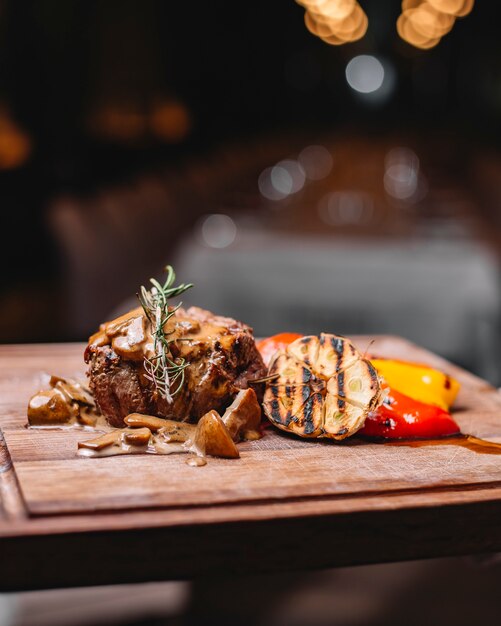 Side view of grilled beef meat served with mushrooms grilled vegetables and sauce on a wooden board