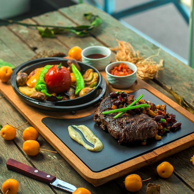 Free photo side view of grilled beef meat served with vegetables and sauce on wooden board