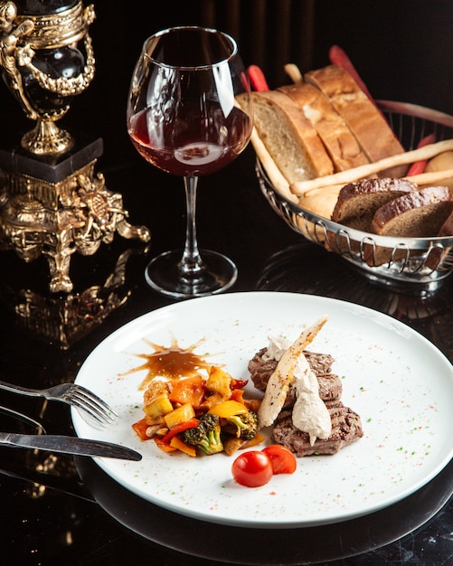 Side view of grilled beef medallion with sauce and vegetables on a white plate on the table