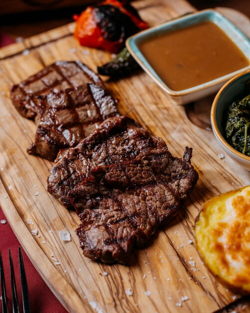 Side view of grilled beef steak with sauce on a wooden board