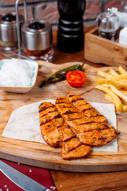 Side view of grilled chicken fillet with french fries on a wooden board