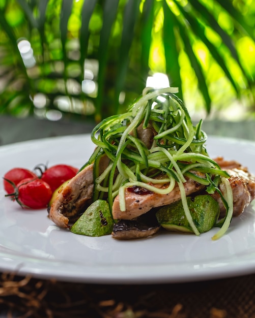 Side view grilled chicken with zukini mushrooms cucumber and tomatoes on a plate