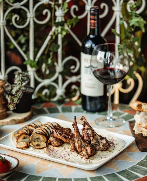 Side view of grilled lamb rib with beef meat and baked sliced potatoe on the table served with bottle of wine