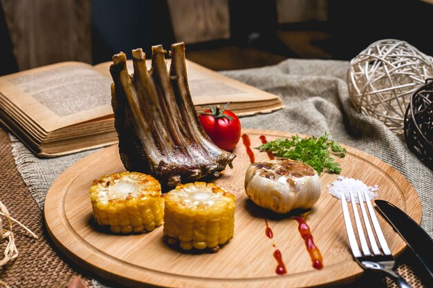 Side view grilled lamb ribs with corn garlic tomato and salt on a board