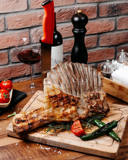 Side view of grilled ribs served with vegetables on wooden board
