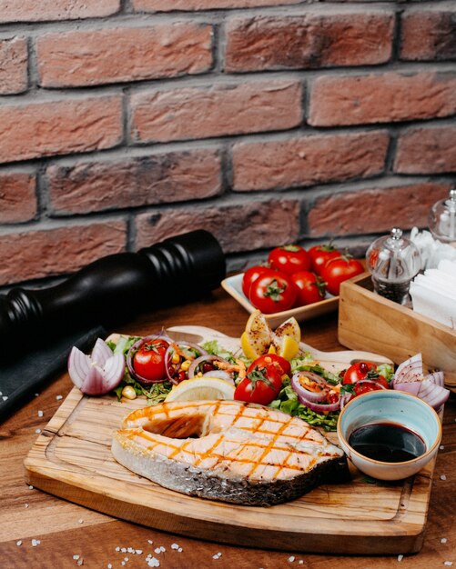 Free photo side view of grilled salmon served with fresh vegetables lemonnd sauce on wooden board