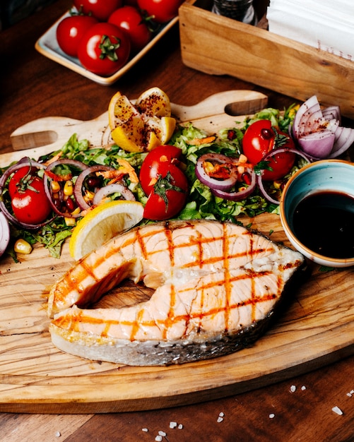 Side view of grilled salmon with fresh tomatoes lemonnd herbs with narsharab sauce on wooden board