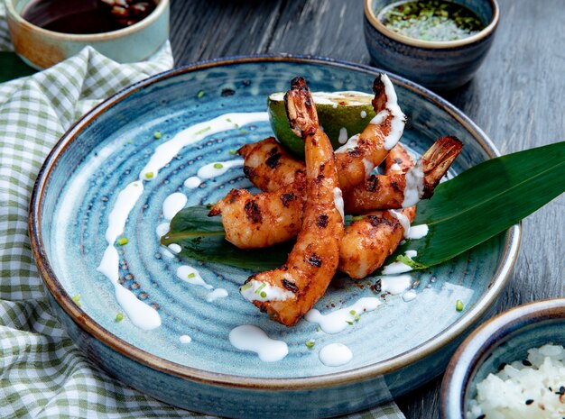 Side view of grilled shrimps with sauce on a plate on wood