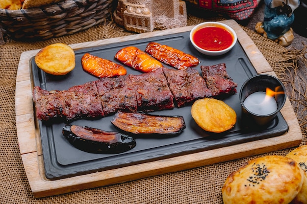 Side view grilled steak with eggplant potatoes bell pepper sauce bread and candle on a board