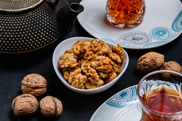 Вид сбоку жареные грецкие орехи с солью и черным чаем на столе