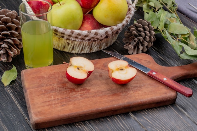 사과 pinecone의 사과 주스 바구니와 나무 표면에 잎 절단 보드에 절반 잘라 사과와 칼의 측면보기