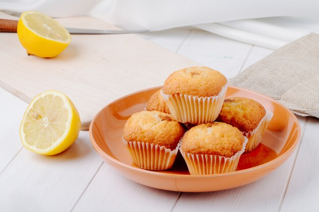 Side view half a lemon on a board with cupcakes on a plate