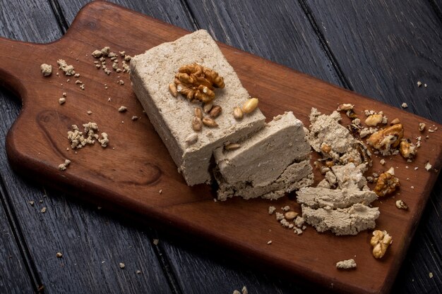 Side view of halva with sunflower seeds and walnuts on a wooden board