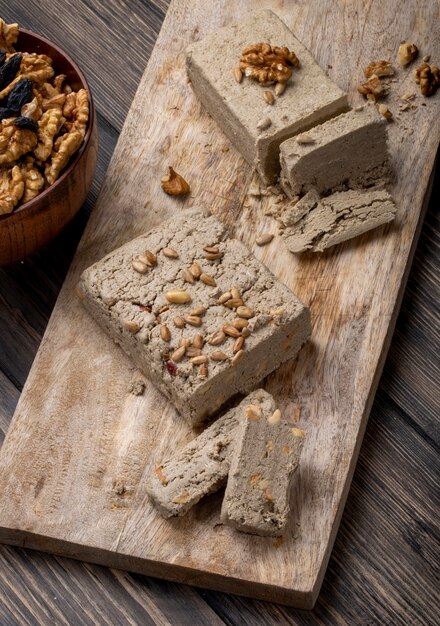 Side view of halva with sunflower seeds and walnuts on a wooden board