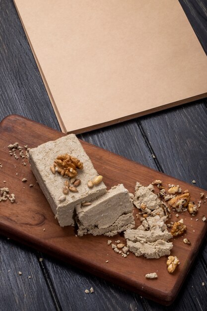 Side view of halva with sunflower seeds and walnuts on a wooden board