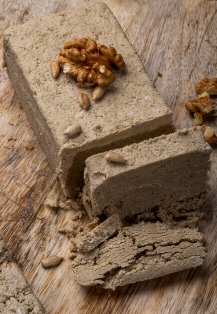 Side view of halva with sunflower seeds and walnuts on a wooden board