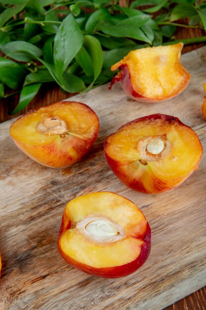 side view of halves of fresh ripe peaches on a wooden cutting board with green leaves on rustic table