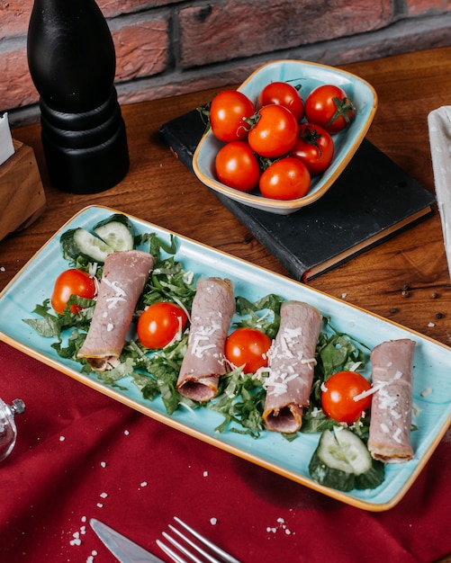 Free photo side view of ham roll withj tomatoes and cucumbers on a plate