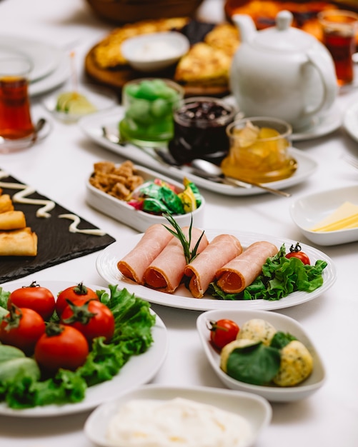 Side view of ham served with fresh herbs vegetables and sauces on the table