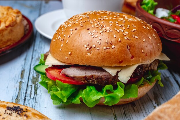 Side view hamburger with grilled meat cheese lettuce and tomato between burger buns