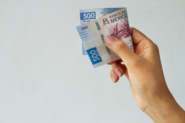 Вид сбоку рука держит мексиканскую банкноту