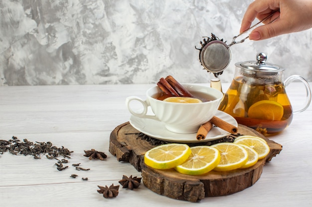 Side view of hand holding tea pot black tea in a white cup around dry tea and leaves on white table