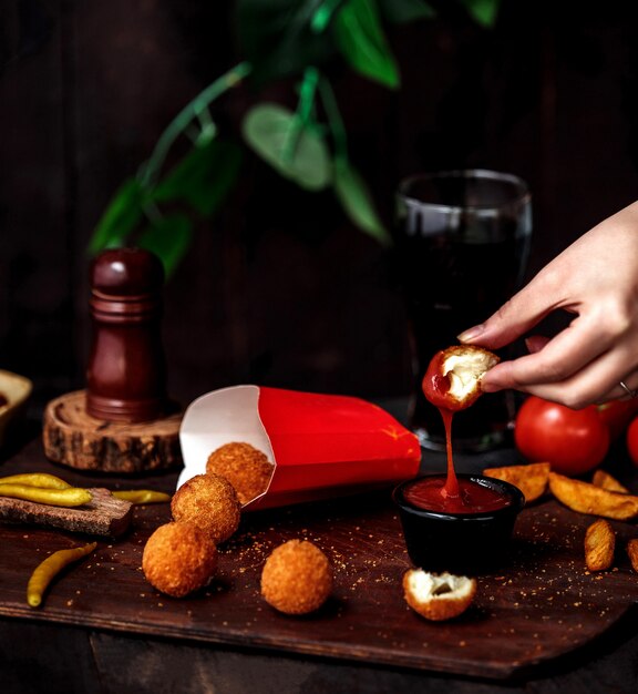 Side view of a hand putting fried cheese ball into ketchup