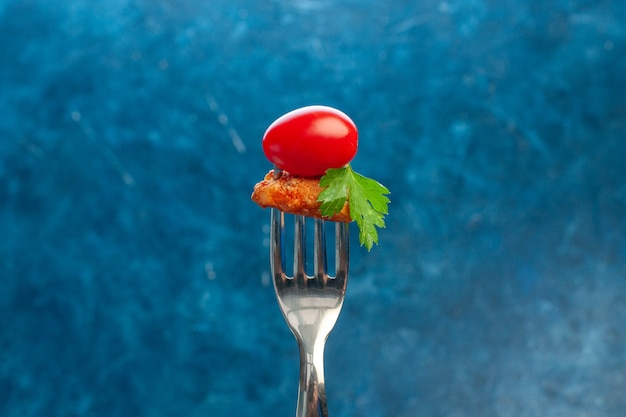 파란색 배경에 포크 토마토와 닭고기를 들고 있는 손의 측면