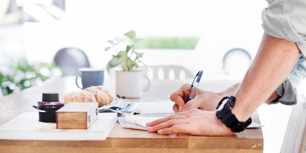 Side view of hand writing on paper on wooden table with bakery