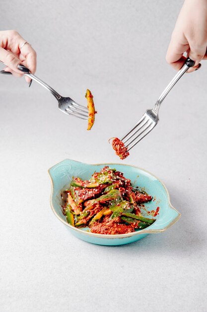 Side view of hands hold forks over the plate with avocado salad with meat and sesame