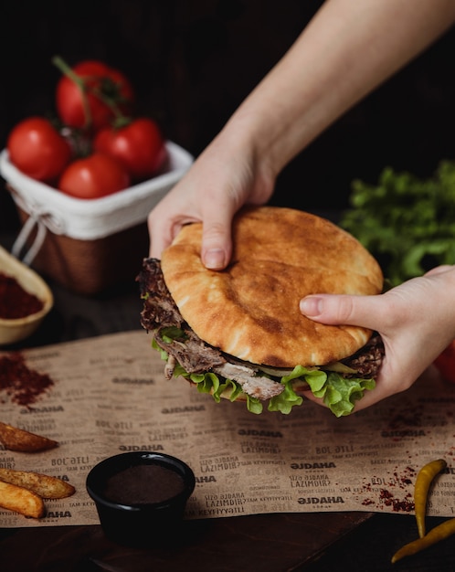 Free photo side view of hands holding doner kebab in pita bread