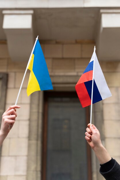 Side view hands holding ukrainian and russian flags