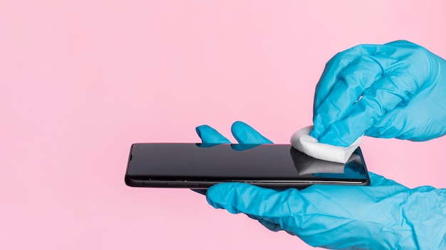 Free photo side view of hands with surgical gloves disinfecting smartphone